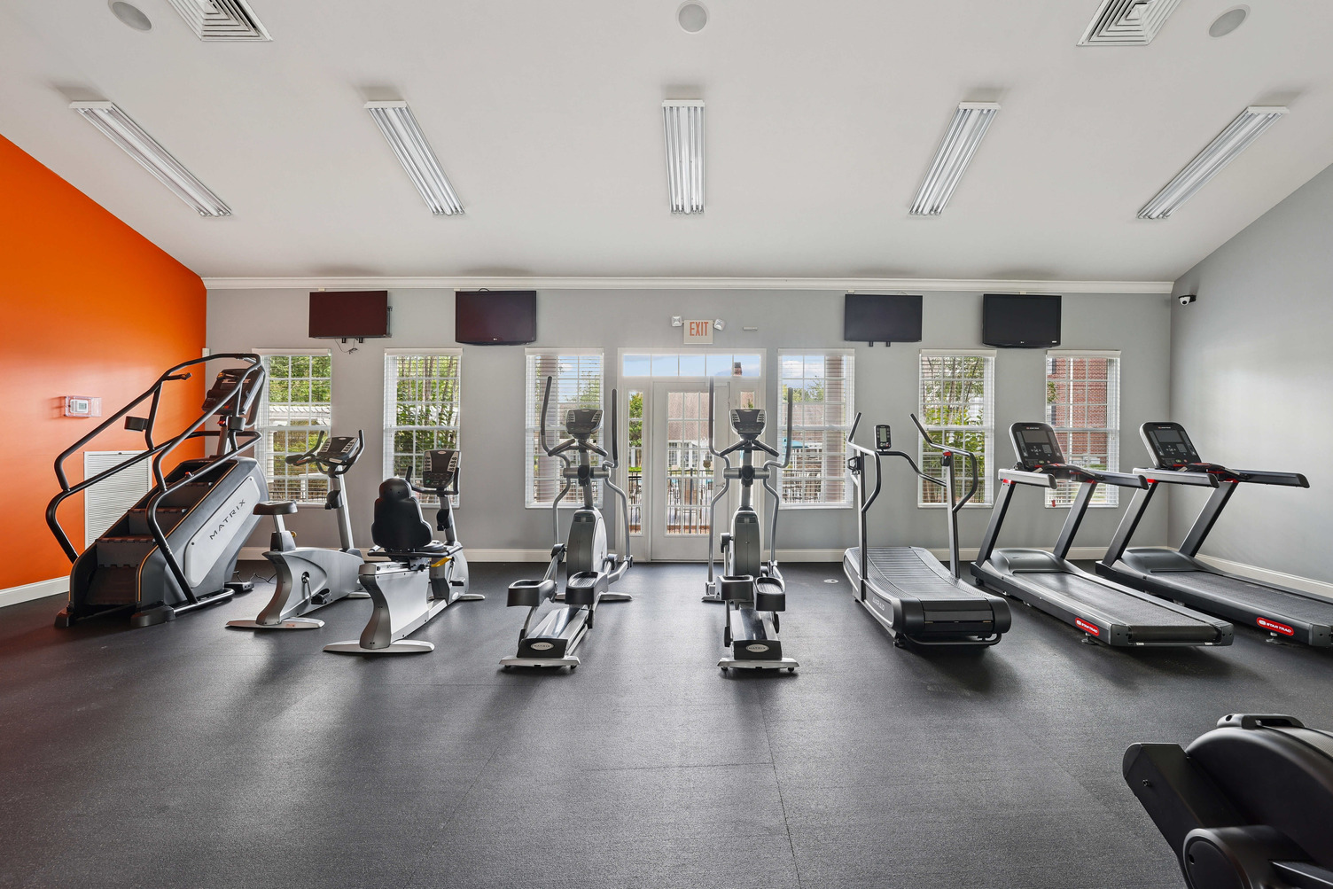 Modern gym with cardio machines, including treadmills, ellipticals, and a stair climber, in a bright room.