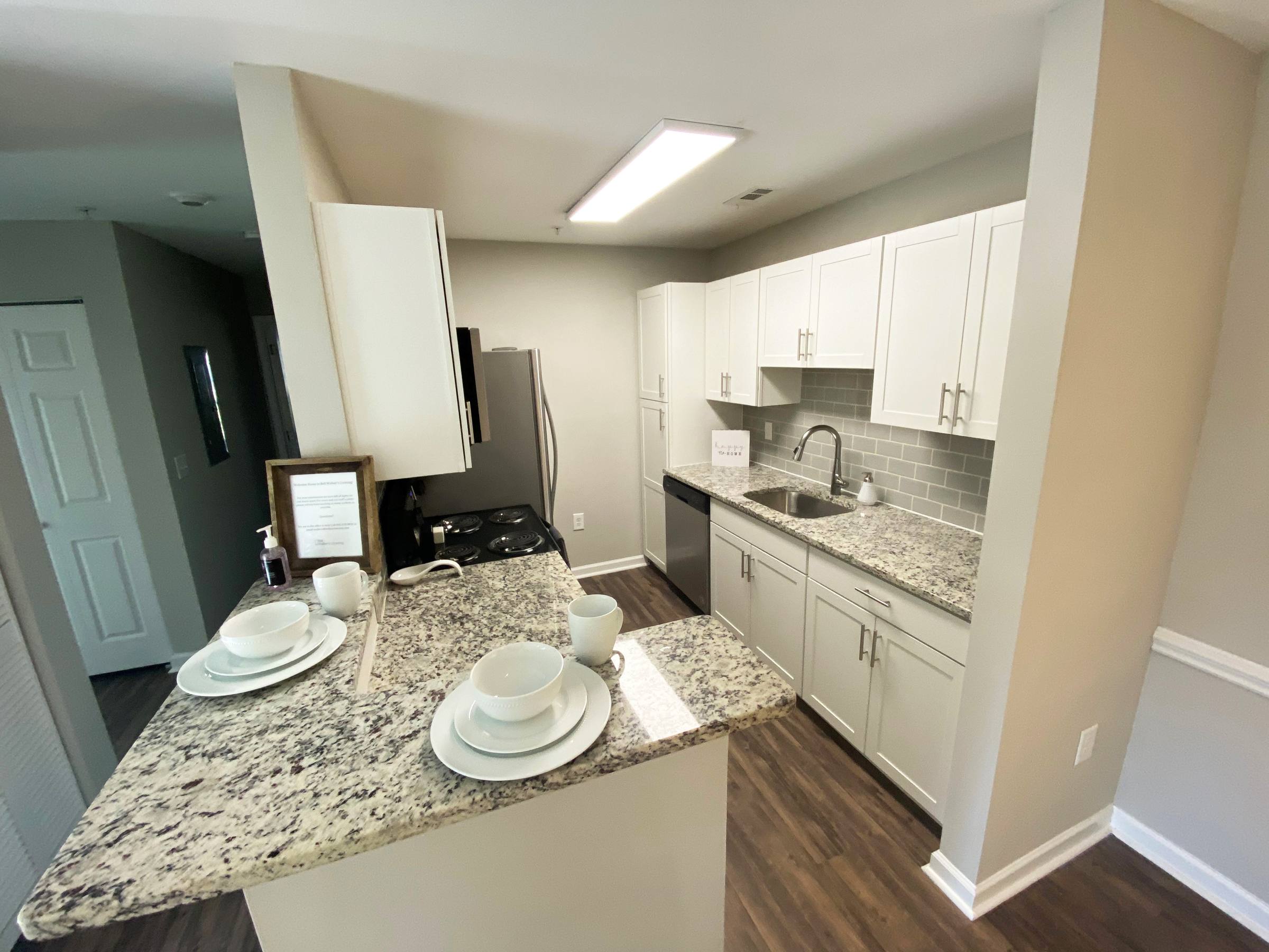 Modern kitchen with white cabinets, granite countertops, and place settings on a breakfast bar.