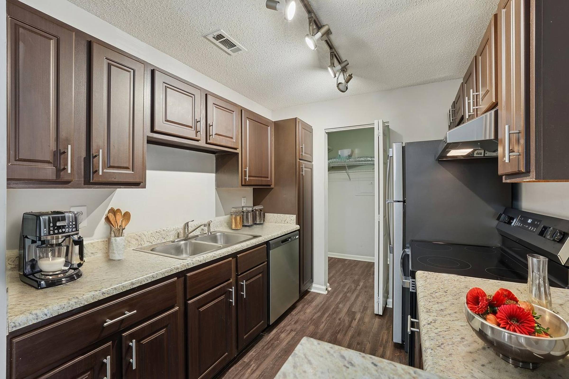 Modern kitchen with dark cabinets, granite countertops, stainless appliances, and a pantry with open doors.
