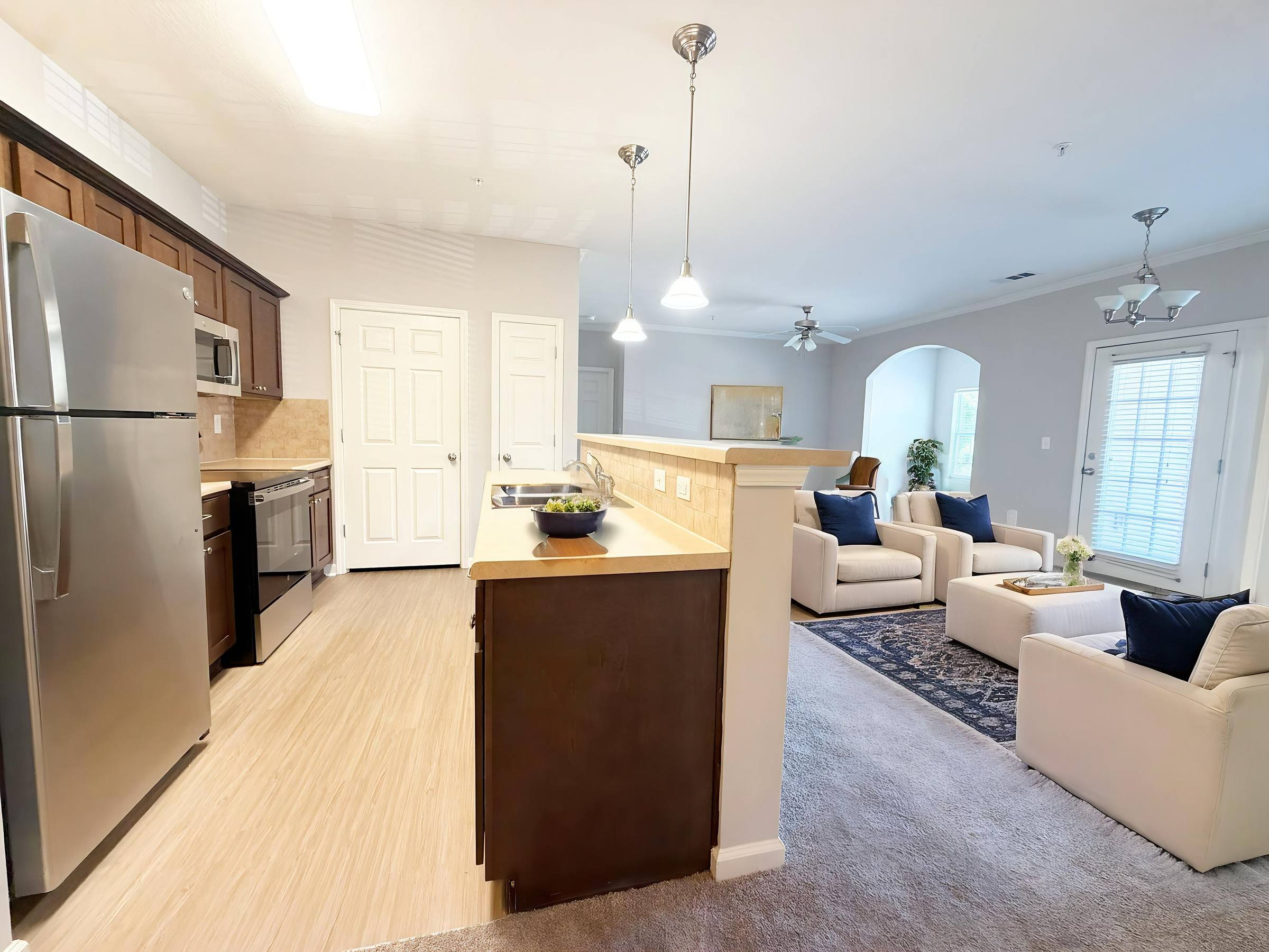 Modern open kitchen and living room with stainless steel appliances, beige walls, and comfortable seating.