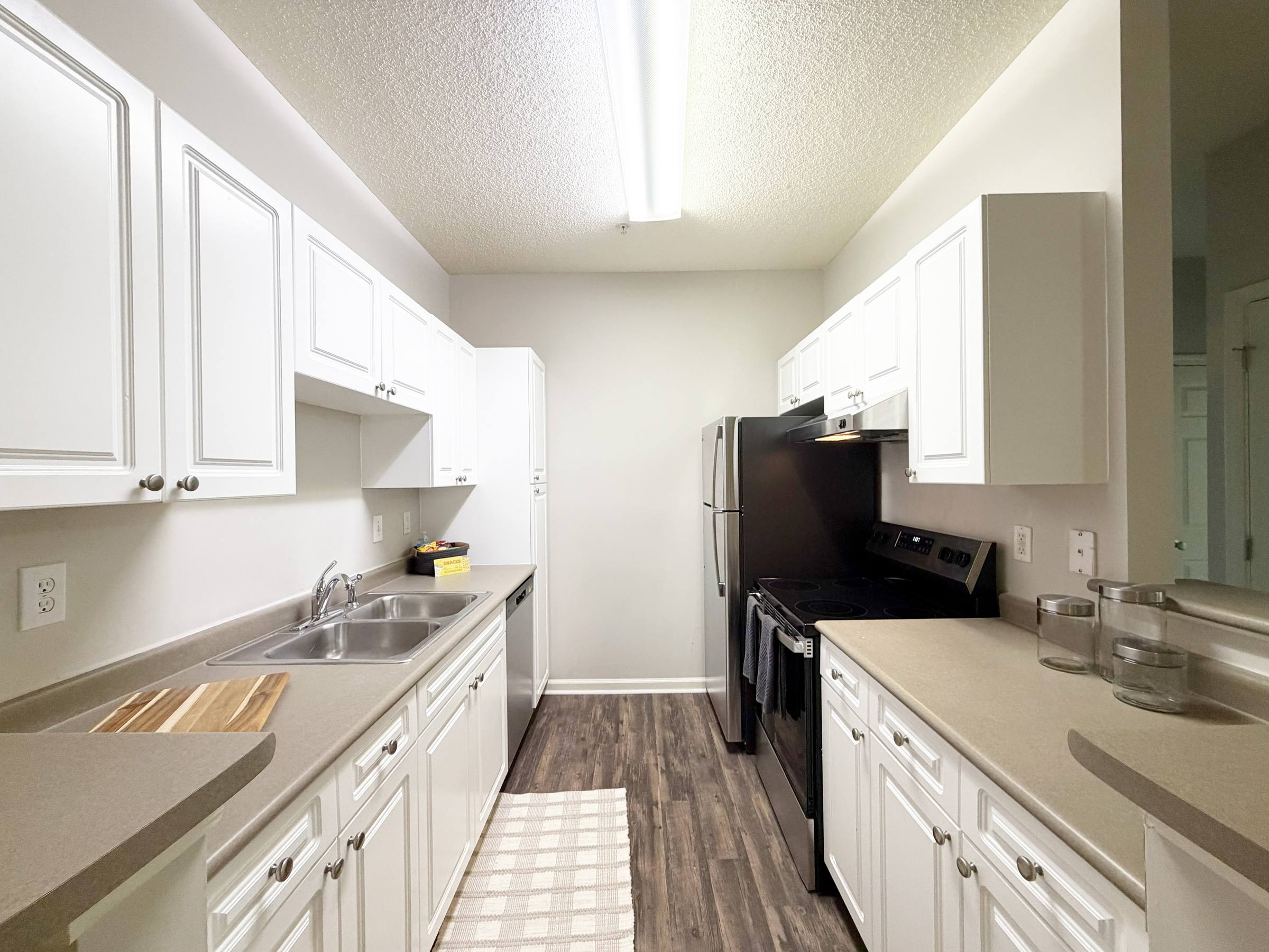 Modern galley kitchen with white cabinets, stainless steel appliances, and wood-look flooring.