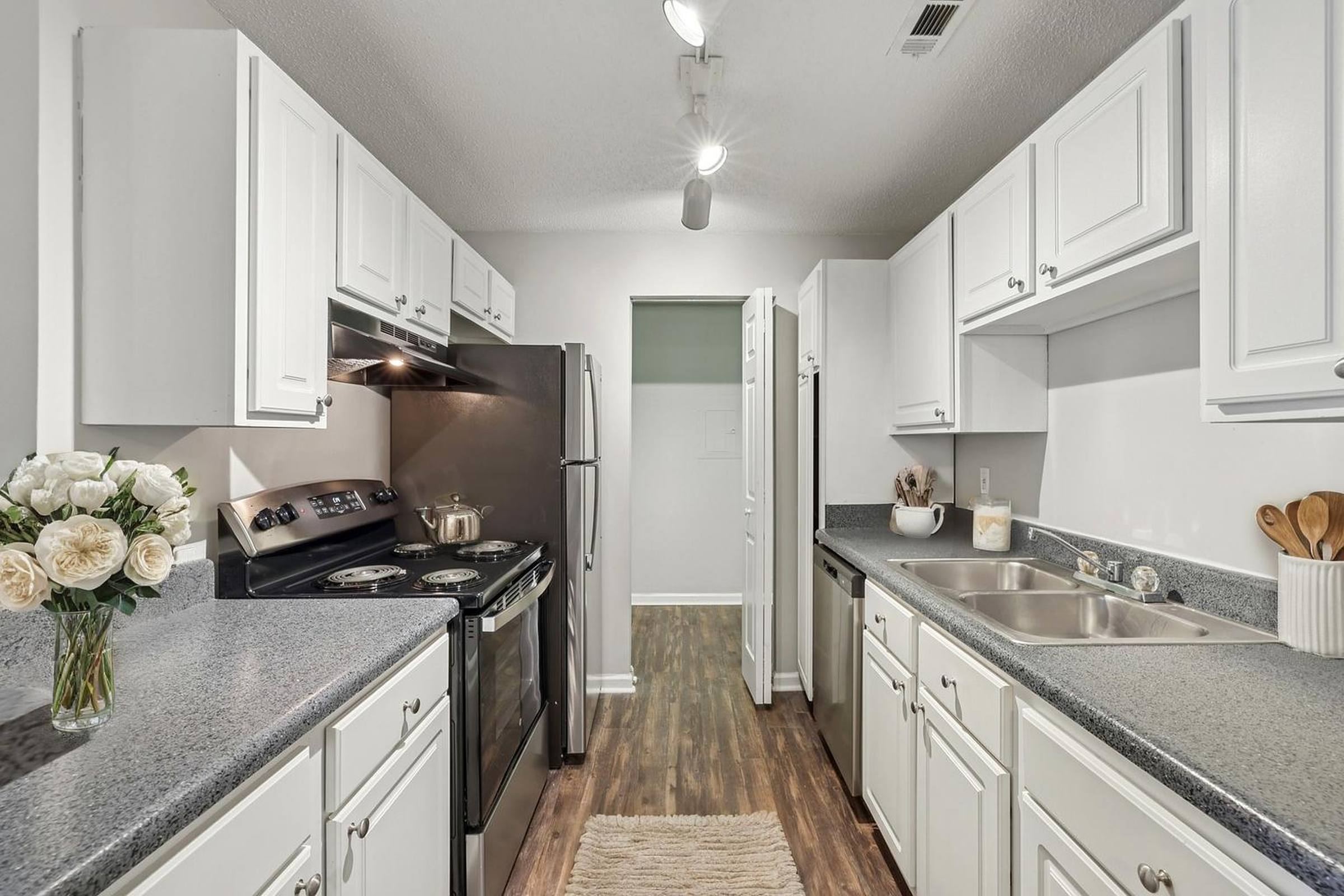Modern galley kitchen with white cabinets, stainless appliances, and a bouquet of flowers on the counter.