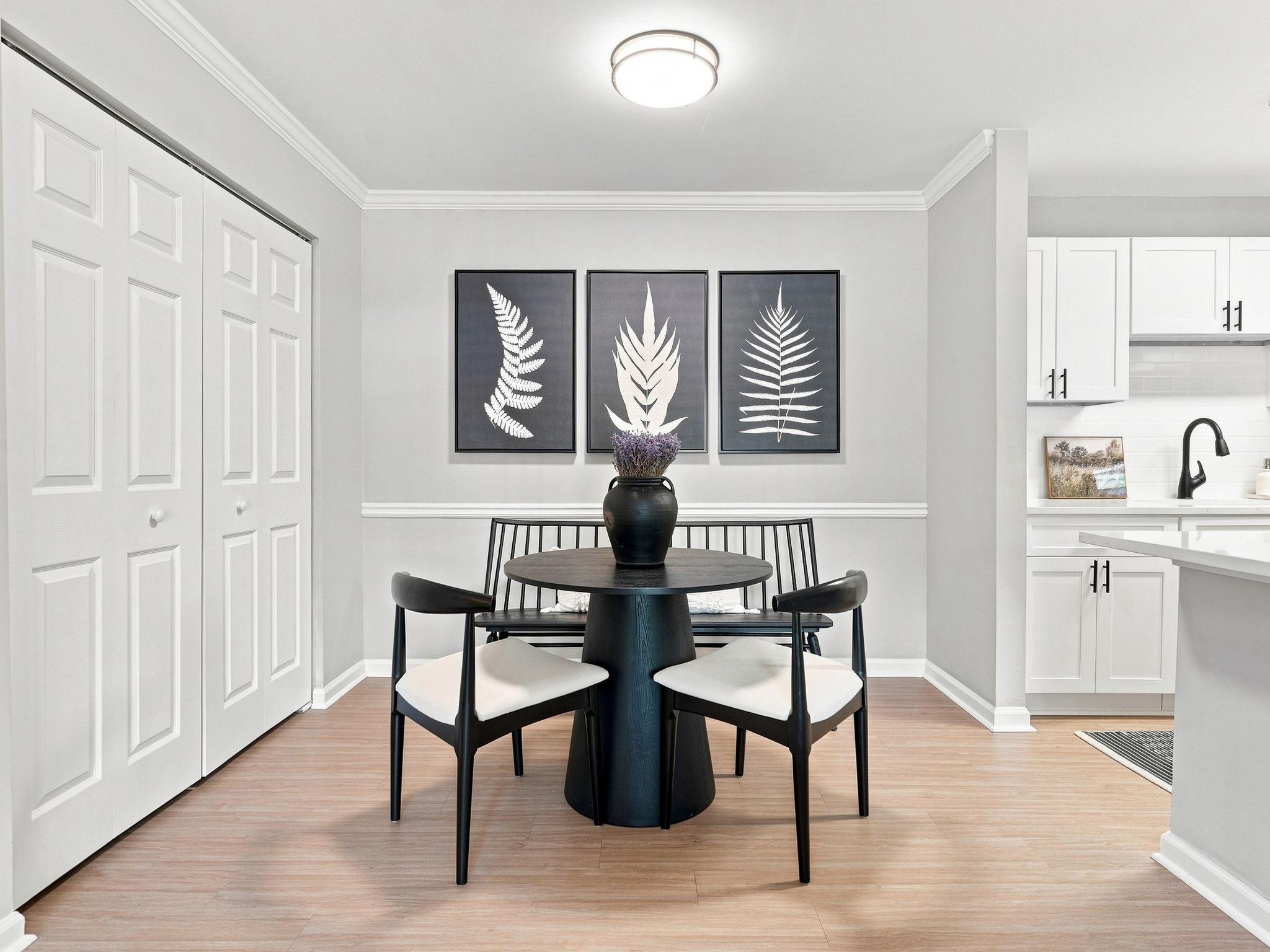 Modern dining area with a round black table, four chairs, a vase, and three fern art prints on the wall.